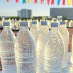 Garrafas de água para hidratação no Carnaval de Brasília 2026, com elementos festivos ao fundo.