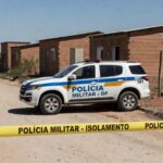 Viatura da polícia em rua da Cidade Estrutural, com fita de isolamento, representando apreensão por suspeita de feminicídio.