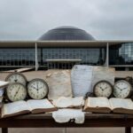 Edifício da CLDF em Brasília com relógios e documentos simbolizando desperdício legislativo em homenagem a corretores de seguros.