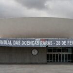 Edifício da CLDF em Brasília com banner atrasado sobre Dia das Doenças Raras, expondo negligência no apoio a pacientes.