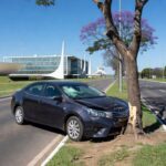 Colisão de carro com árvore na Via W2 Sul em Brasília, veículo danificado ao lado da avenida.