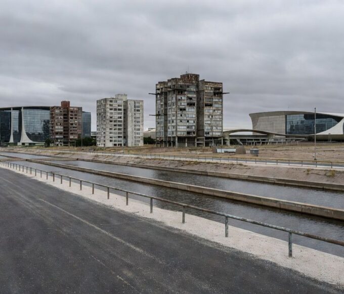 Obra hídrica tardia no Lago Sul, DF, com reservatórios e tubulações em paisagem urbana negligenciada.